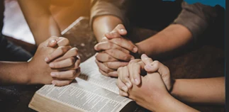Hands folded in prayer over an open Bible